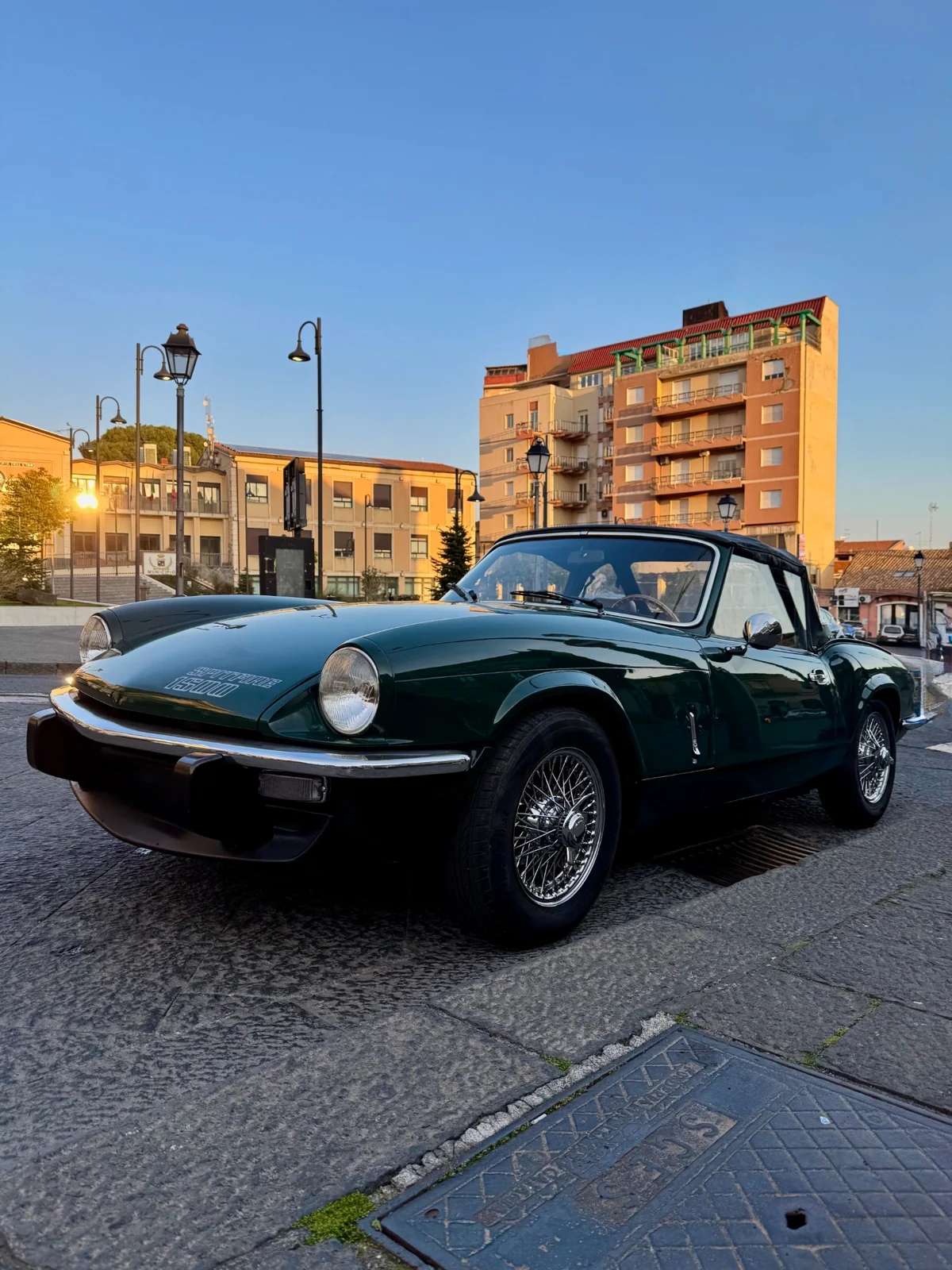 La Triumph verde inglese in città, tra architettura e luce del tramonto